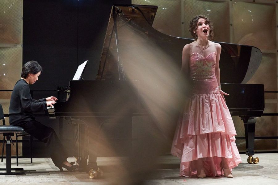 Ein Studentin in einem bunten Kleid singt auf der Bhne, neben ihr eine Studentin am Klavier