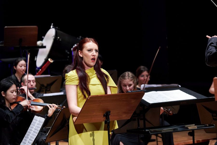 Eine S?ngerin in einem gelben Kleid steht vor einem kleinen Ensemble und singt