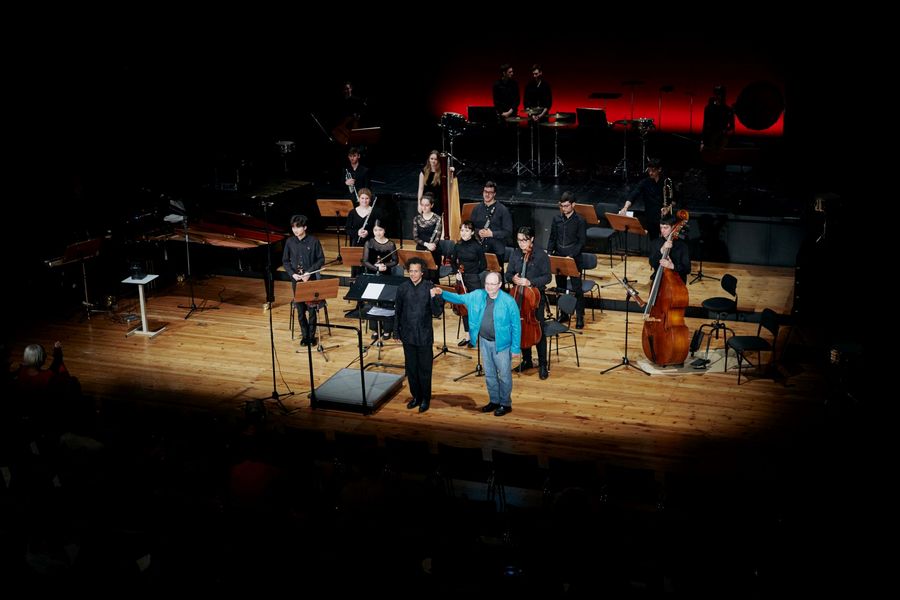 Ensemble, Dirigent und Mann in blauer Jacke nehmen auf der Bhne den Applaus stehend in Empfang