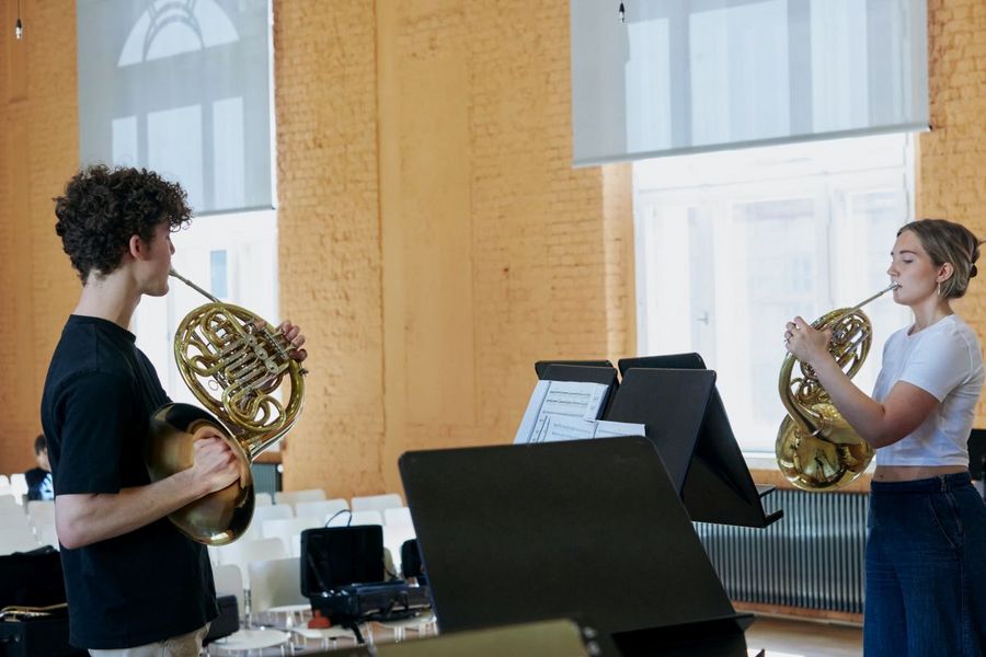 Eine Studentin und ein Student stehen sich gegenber und spielen Horn
